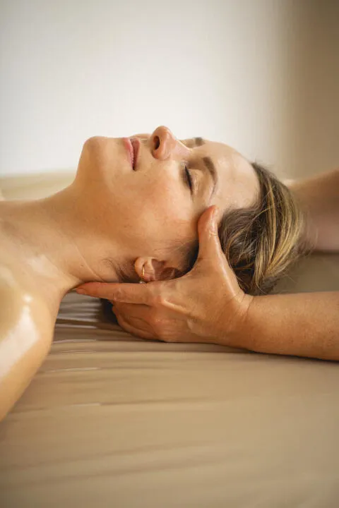 A close-up shot of a woman receiving a professional head and neck massage with her eyes closed in a serene spa setting.