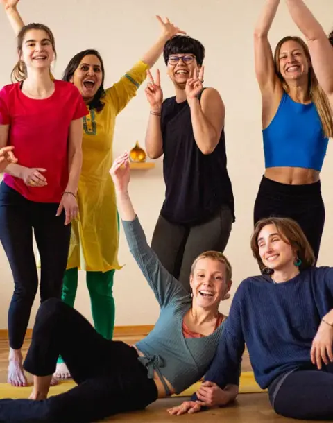 A group of cheerful women posing and laughing together in a bright yoga studio.