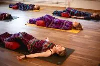 Group of people practicing Shavasana yoga pose with blankets and bolsters.