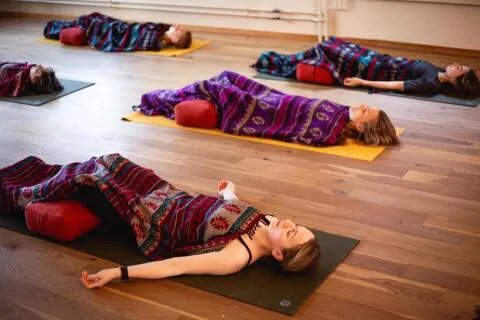 Group of people practicing Shavasana yoga pose with blankets and bolsters.