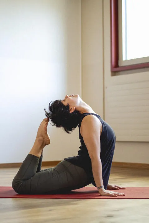 Woman in a king cobra yoga pose on a red mat in a studio.