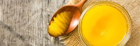 Freshly prepared golden ghee, a staple in Ayurvedic cooking and wellness, displayed with a wooden spoon.