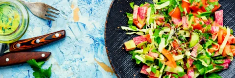 Healthy vegan salad with fresh vegetables and microgreens served on a black ceramic plate.