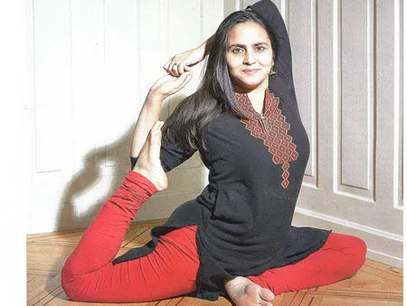 Yoga teacher Poonam Stecher Sharma holding a one-legged king pigeon pose on a wooden floor.