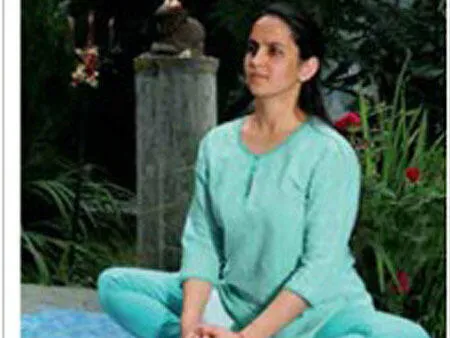 Yoga teacher Poonam Stecher Sharma sitting on a mat in a meditative pose outdoors.